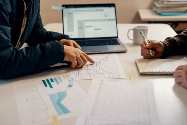 Two people discussing papers and charts at a desk.