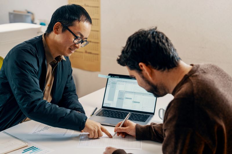 Accountant or financial advisor having casual meeting with client in an office setting. They are looking at paper documents and using a laptop