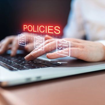 Hands typing on a laptop with the word 'POLICIES' floating above.