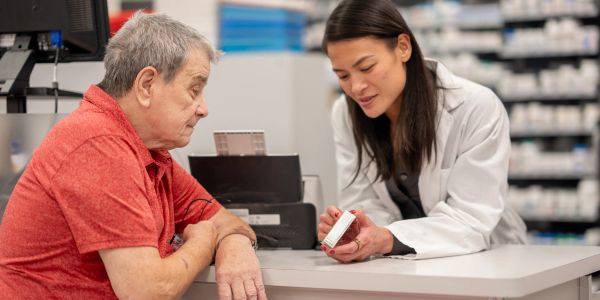 Paciente escucha a farmacéutica en mostrador.