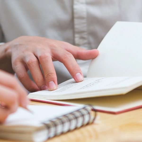 Person reading a book and another writing in a notebook.