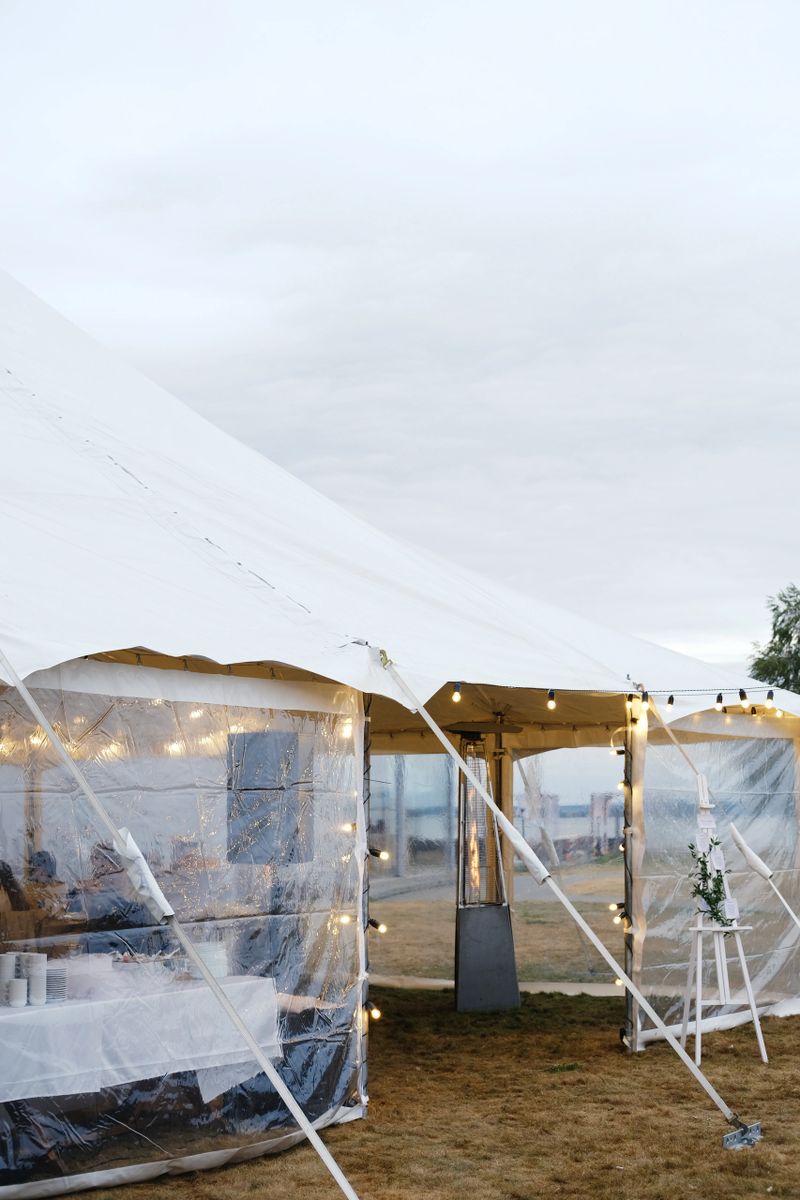Spacious outdoor tent features transparent sides and string lights, set on grassy area, providing inviting ambiance for events and celebrations in nature
