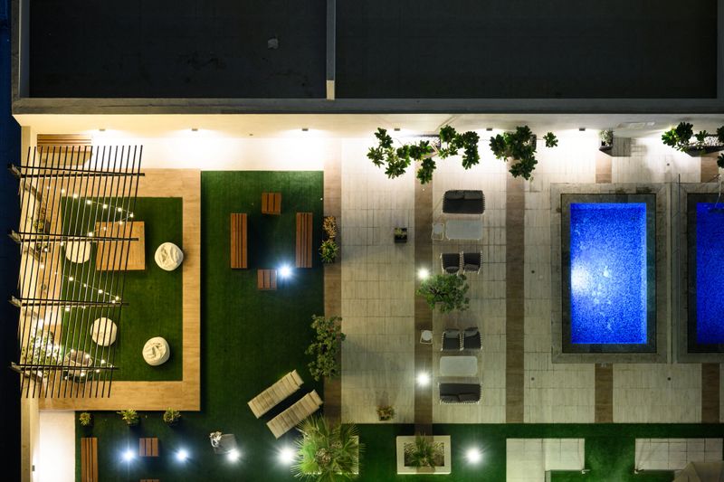 Glowing blue and green lights illuminate the contemporary architectural elements of a luxury hotel rooftop in Dubai, surrounded by lush greenery and potted plants creating a serene, relaxing ambiance.