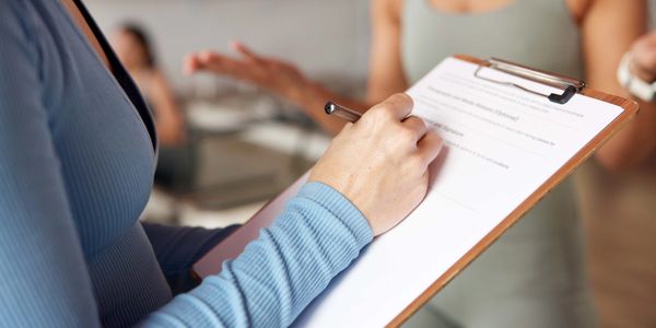 Person filling out a form on a clipboard during a group discussion.