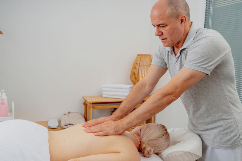 Male therapist performs a back massage on a Caucasian woman in a calming spa setting, featuring towels and soft lighting for relaxation