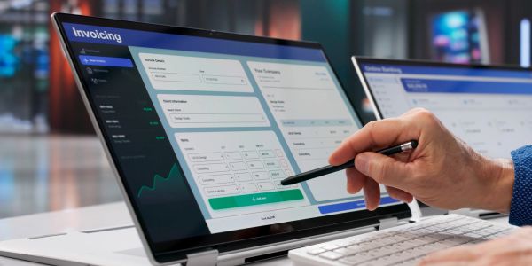 Person using stylus on laptop screen showing invoicing software interface.