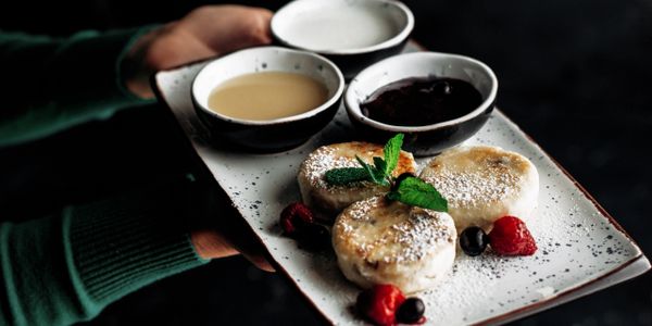 Plate with three cheesecakes, berries, and sauces, held by a person in a green sweater.