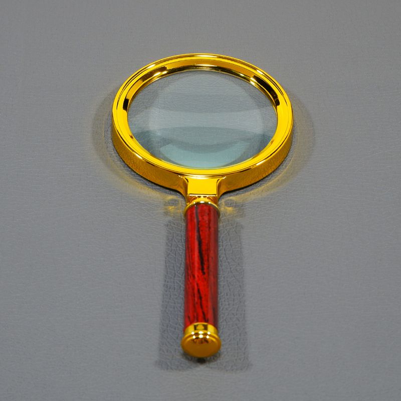 Elegant magnifying glass featuring a striking golden bezel and a contrasting polished red wood grip sits vertically on a smooth, grey backdrop, perfect for concepts related to scrutiny, finding small details, or deep analysis.