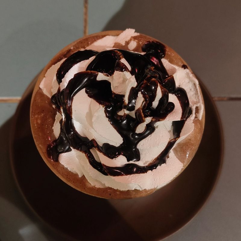 Top view of a hot chocolate drink topped with whipped cream and chocolate syrup creating a cozy dessert moment.