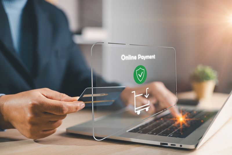 Man paying online with credit card while typing on laptop, secure ecommerce checkout interface with shield icon and cart, digital fintech transaction for cashless shopping and banking services.