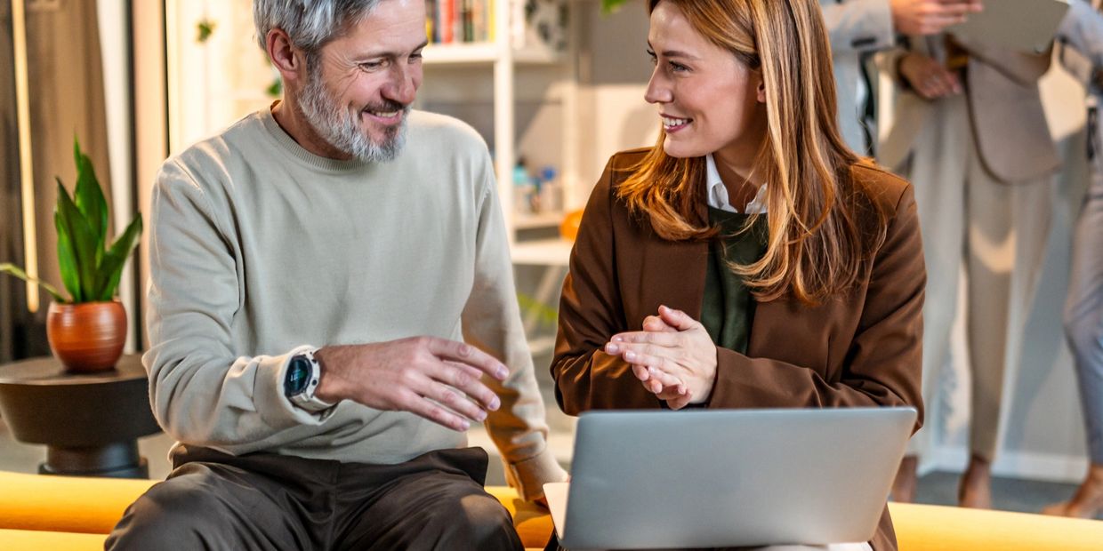 Two colleagues happily discussing work with a laptop in an office setting.