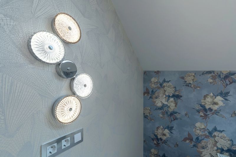 Close-up of a contemporary lighting installation featuring four round glass wall lamps with different textures, mounted on a light patterned wallpaper in a luxury residential interior.