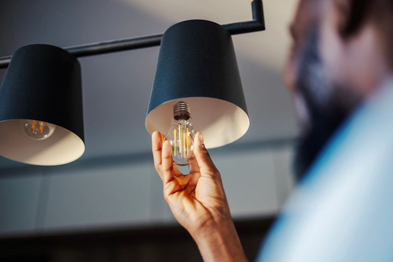Adult male hand screwing in a new led light bulb into a stylish pendant light fixture, focusing on home maintenance, energy efficiency, and diy home improvement
