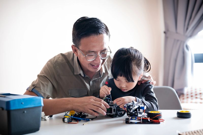 The young Asian girl and her father create lasting memories while constructing their robot toy together in the living room.