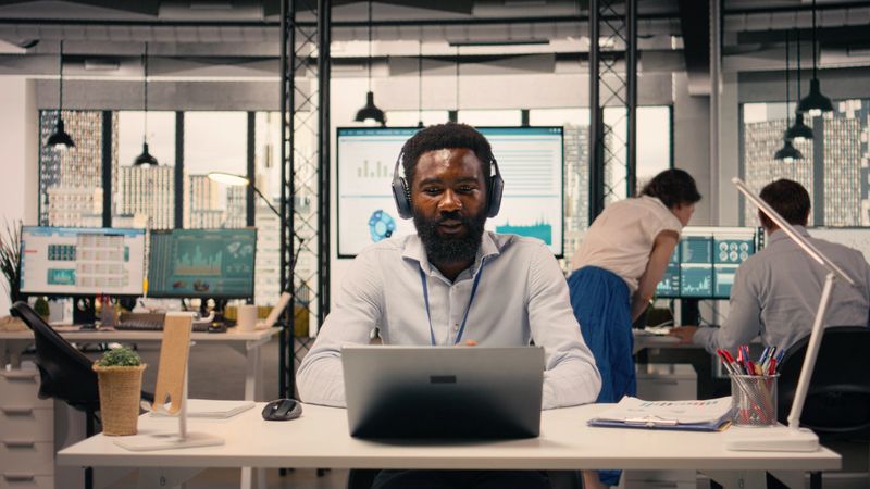 Black professional attending video conference with headphones in modern office. Business work scene showing charts and data analysis during online briefing, transparency and communication.