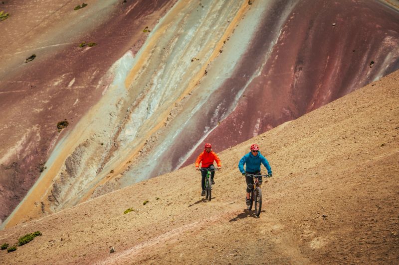 Mountain bikers free-rides track on colourful sandstone mountains, bikepacking in Vicuna or Rainbow Mountain on Ausangate Trek