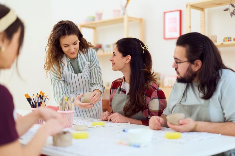 A friendly pottery workshop where adults collaborate on clay projects. An instructor guides a small group as they shape, refine, and decorate bowls, fostering creativity, teamwork, and hands-on learning in a cozy studio.
