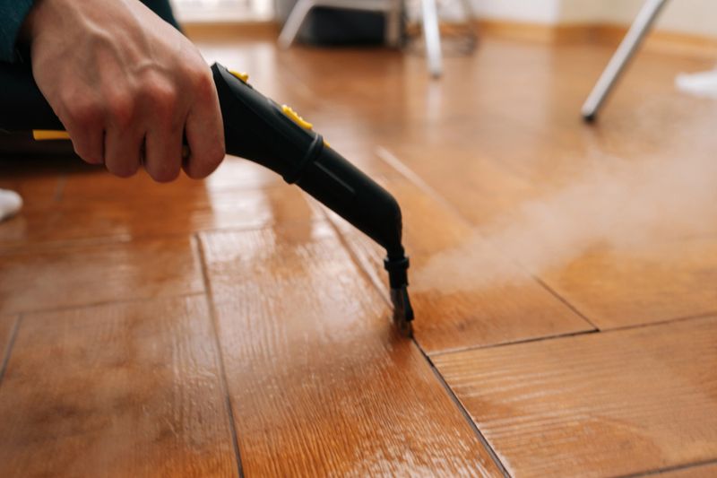 Cleaning service employee sanitizing floor with a steam machine, maintaining household cleanliness and effectively eliminating grime from tiled surface with hot steam. Concept of domestic hygiene.