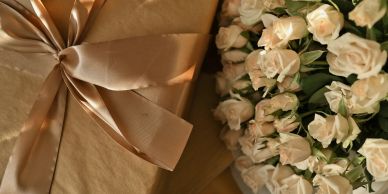 Elegant golden-wrapped gift with a bow beside white roses.