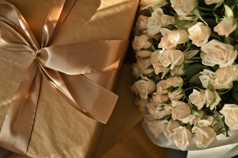 A beautifully wrapped present sits beside a lush arrangement of soft, creamy roses, evoking a sense of luxury and celebration