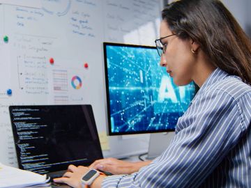 Woman coding at a computer with AI displayed on a monitor.