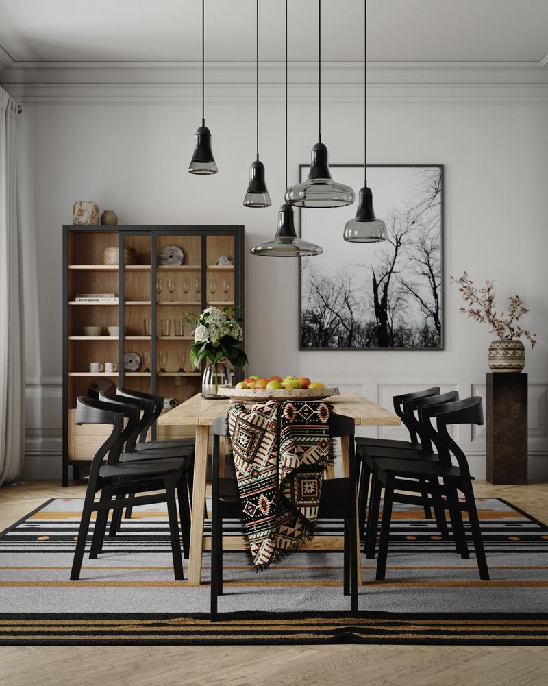 Digitally generated vertical portrait of a modern dining table set in a stylish Scandinavian apartment. Black glass pendant lights hang above a wooden table surrounded by black chairs, with a patterned throw, bowl of fresh fruit and flowers adding warmth. A glass cabinet and framed tree photograph complete the elegant, design-focused interior.