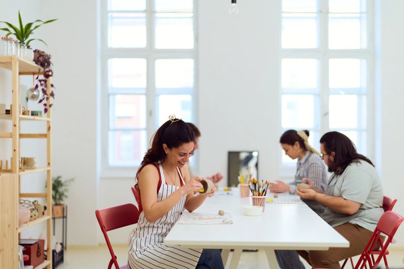 A bright, collaborative craft workshop where friends craft and paint at a long white table, surrounded by supplies and airy windows, showcasing creativity, teamwork, and a cozy, modern studio vibe.