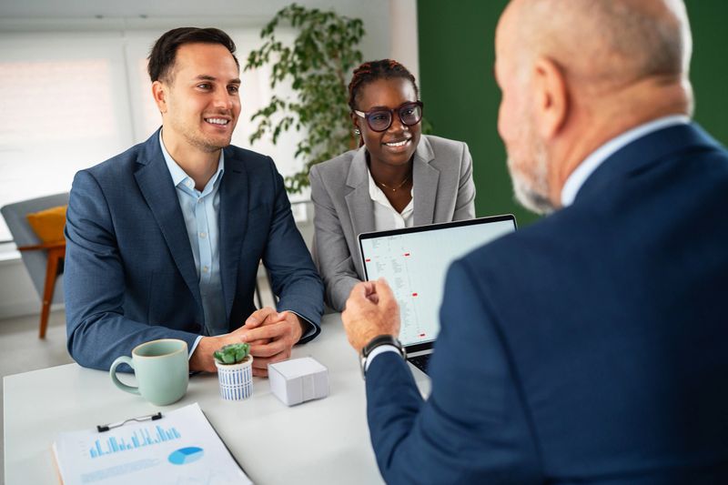Young diverse couple discussing financial plans with a senior professional in a bright office environment.