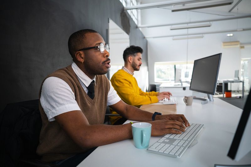 Diverse business professionals collaborating in a modern coworking space, focusing on computers for office productivity