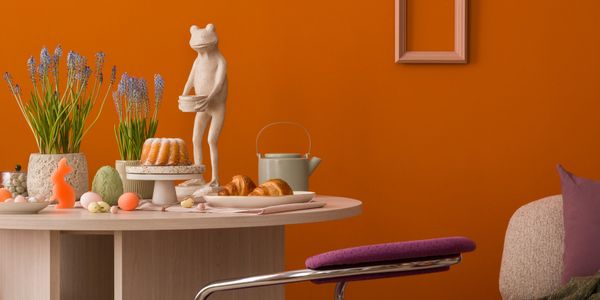 Cozy table setting with pastries, flowers, and unique decor against an orange wall.