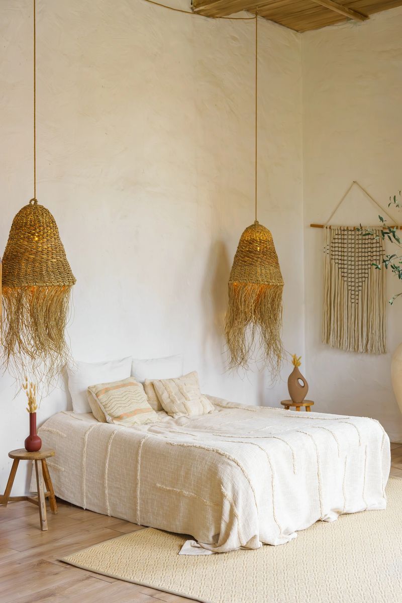 Stylish boho bedroom interior with cozy bed, wicker pendant lamps, neutral colors and natural textures. Minimalist home decor concept with calm atmosphere and modern bohemian design.