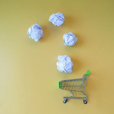 Mini shopping cart with crumpled paper balls on a yellow background.