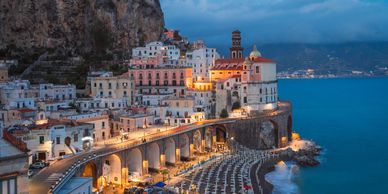 A coastal town at twilight with illuminated buildings and a beach.