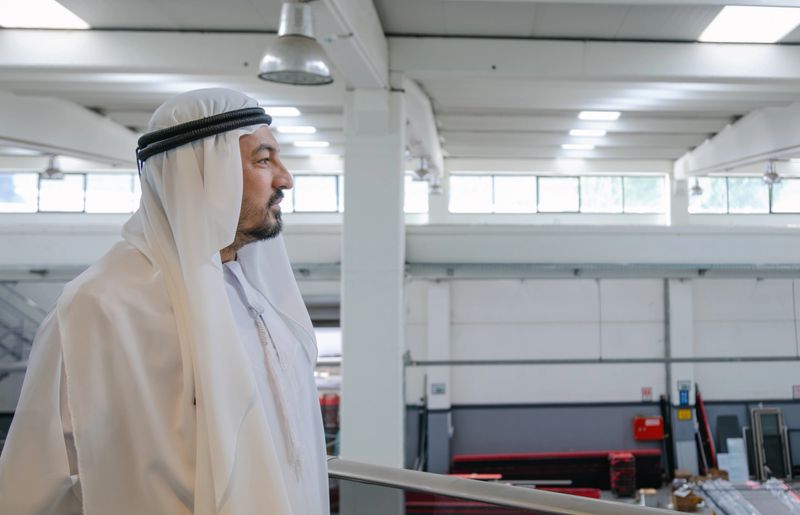 Industrial leadership scene showing Middle Eastern male executive wearing traditional kandura standing at elevated factory platform while overlooking anc checking aluminium joinery and facade systems manufacturing area, emphasizing international business management, engineering industry, industrial inspection and modern metal production environment