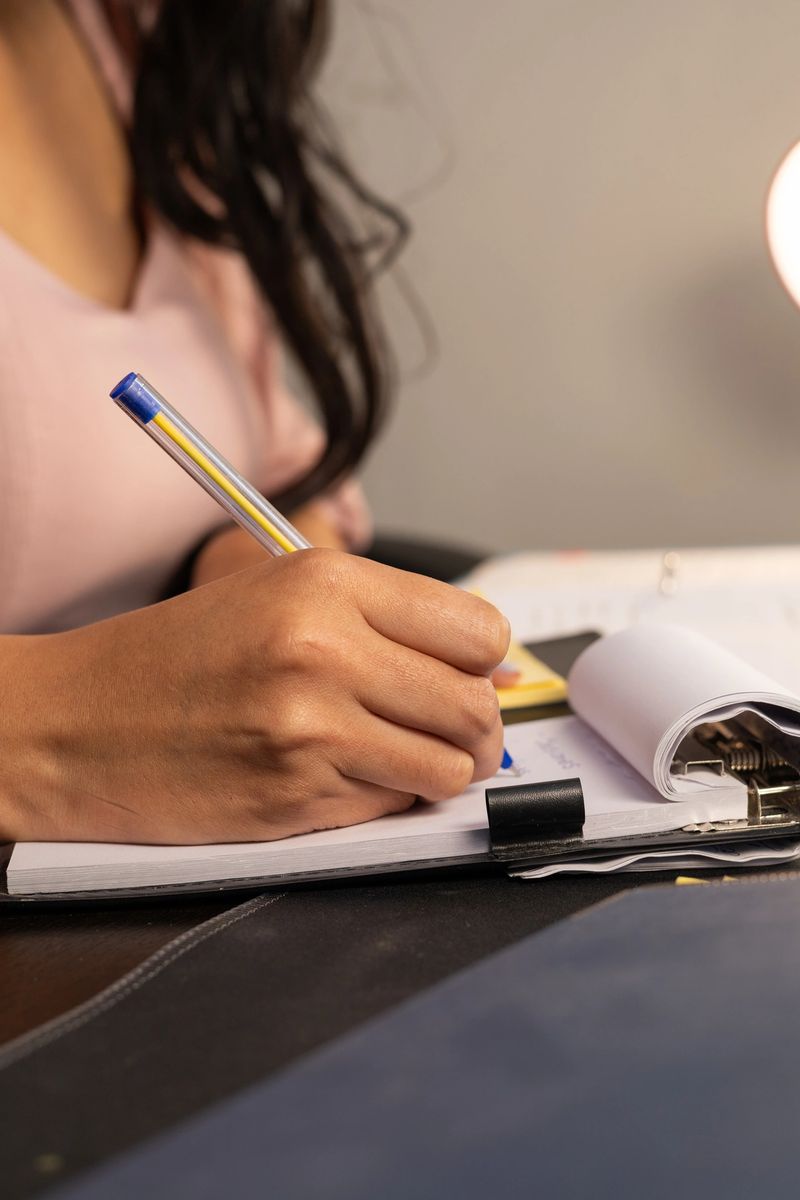 Close view of hands flipping sticky notes and writing on a notepad while working in an organized office environment.