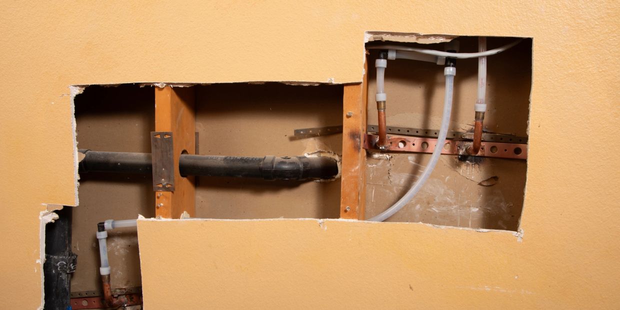 Exposed plumbing and pipes behind a cut-out wall.