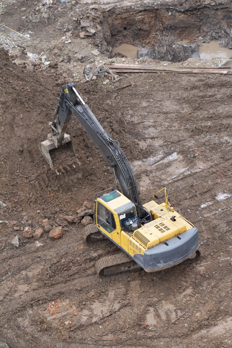 A yellow hydraulic excavator is digging into a pile of dirt on a muddy construction site. Concept of earthworks and site preparation.