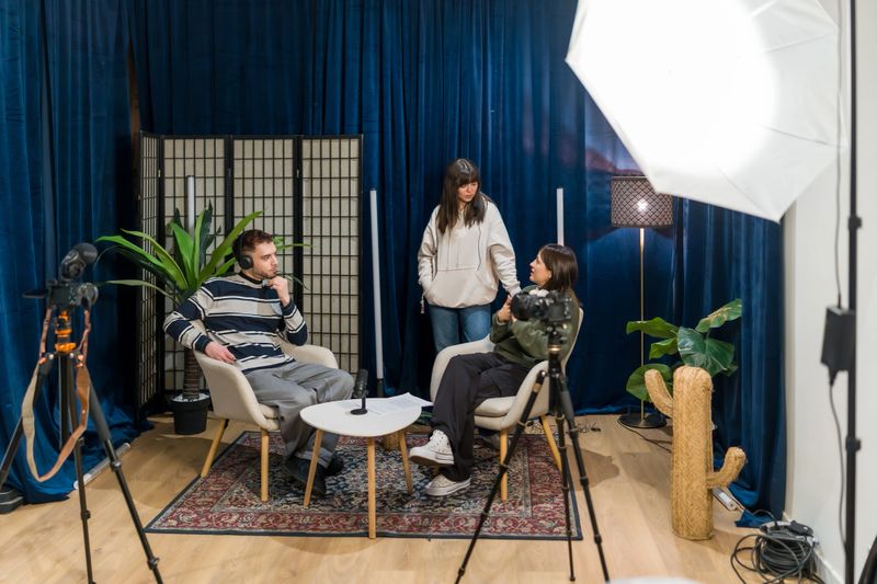 Three young adults collaborating in a professional studio to record a podcast episode with microphones, cameras, lighting and headphones, planning, chatting and filming content