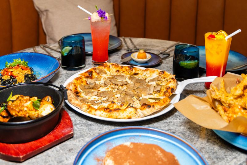 Gourmet dining table with truffle pizza, seafood pasta, cocktails, and appetizers in restaurant setting. Italian cuisine and fine dining concept.