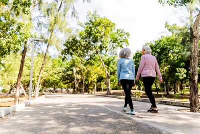 Two elderly women walking in a sunny park.
