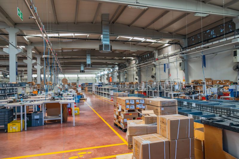 Wide angle view of organized manufacturing facility showing assembly line equipment, workstations, storage pallets and logistics workflow in large industrial factory hall, clean production environment highlighting efficiency, technology and supply chain operations with copy space