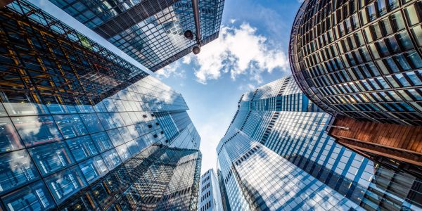 Looking up at modern skyscrapers with glass facades against a blue sky.