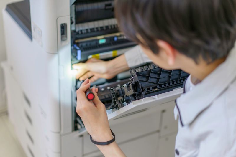 Close-up of a young Japanese man's hands performing maintenance on a copy machine in the office