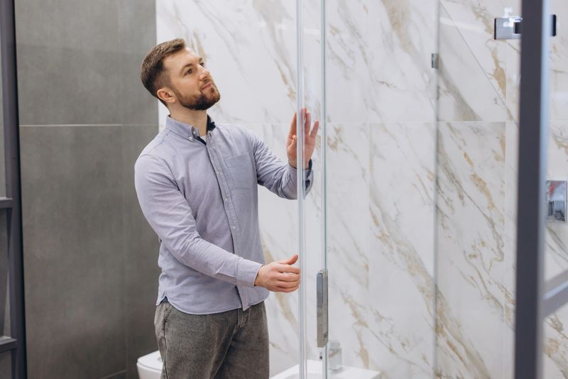 Man examining a glass shower door, seeking inspiration for updating his bathroom with new design elements and innovative construction ideas