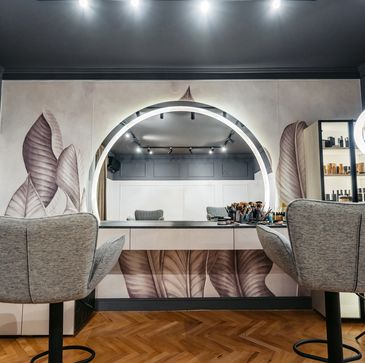 Modern makeup station with illuminated mirror and cozy chairs.