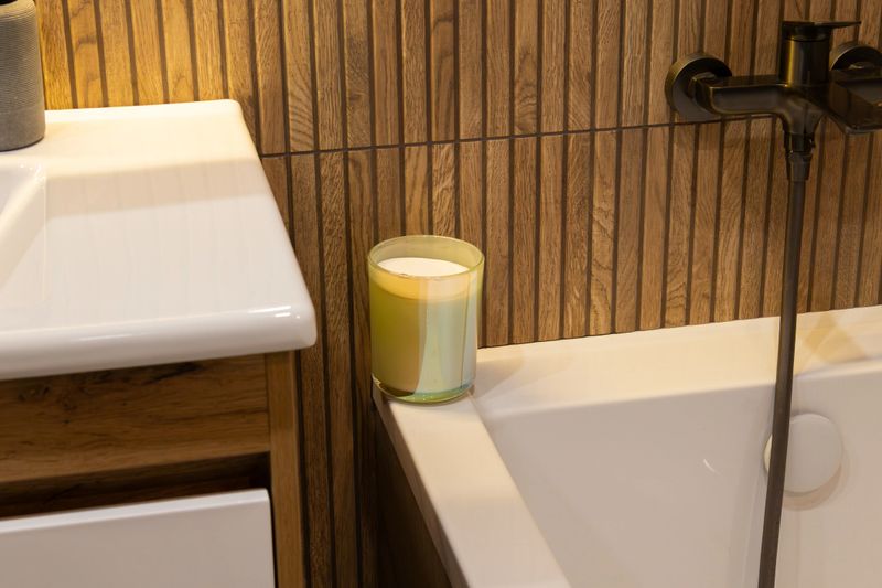 A warm, inviting bathroom showcases a stylish candle resting beside a sleek bathtub, creating a tranquil atmosphere perfect for unwinding
