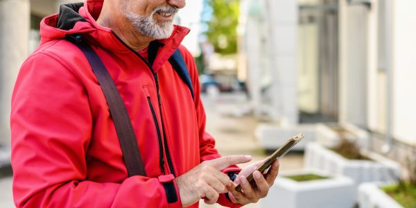 Man wearing red jacket using smartphone outdoors.