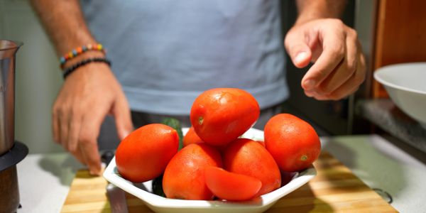 Fresh Roma tomatoes in a bowl with a person's hands nearby.