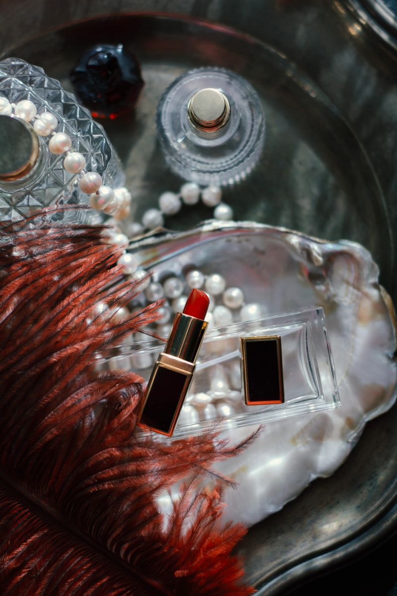 Luxury beauty flat lay: deep red perfume, gold lipstick, black case on iridescent mother-of-pearl tray with natural pearls. Soft dreamy lighting, romantic glow, feminine elegance for high-end cosmetics and fragrance concepts.