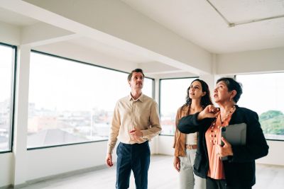 Three professionals inspecting an empty office space with large windows.